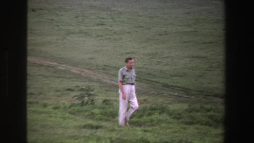 The man reaches the lower edge of the grassy area, framed by visible 8mm borders and a muted South African landscape.