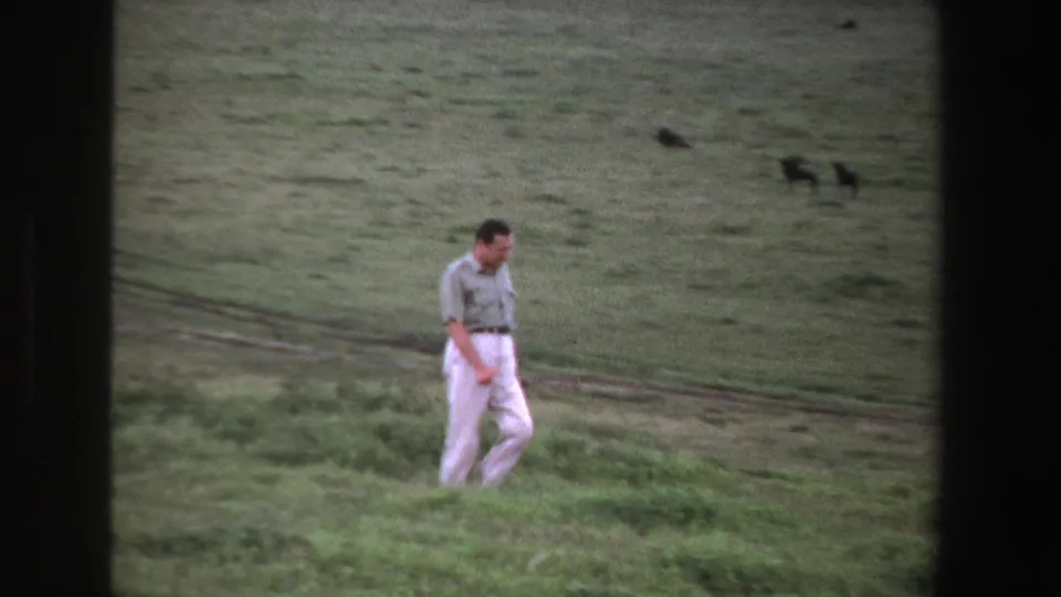 The man continues across uneven grass in South Africa, 1969, with soft-focus open ground and a dirt track behind him.