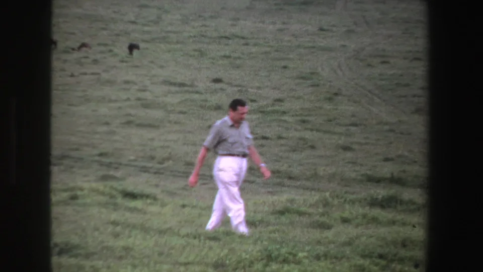 The man continues across the South African grassland, with scattered wildebeests visible in the background on 8mm film.