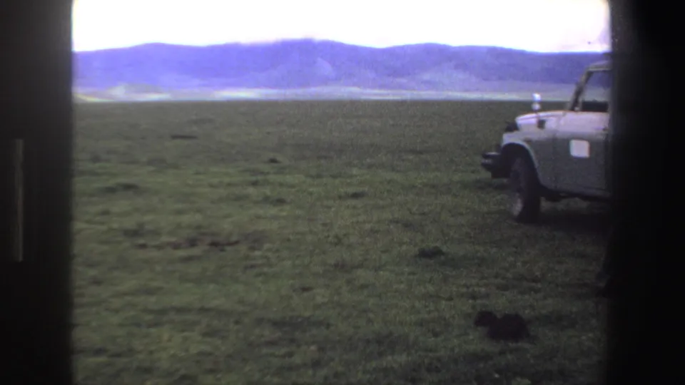 1969 South Africa home-movie frame showing open grassland with the grey station wagon partly cropped at right.