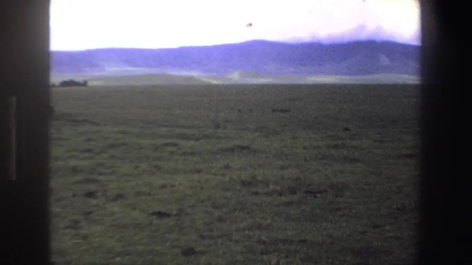 1969 South Africa home-movie frame looking across broad grassland toward a hazy blue mountain ridge.