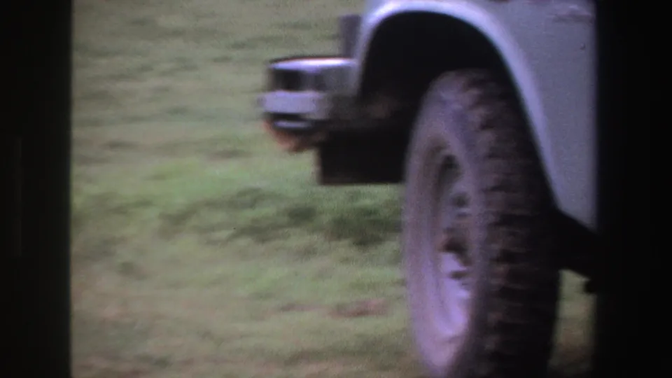 The 8mm view shifts to the side and wheel of an off-road vehicle standing on grassy terrain in South Africa.