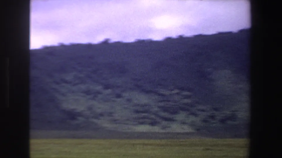 Rolling green hills and open field appear beneath a purple sky in 1969 South Africa 8mm footage.