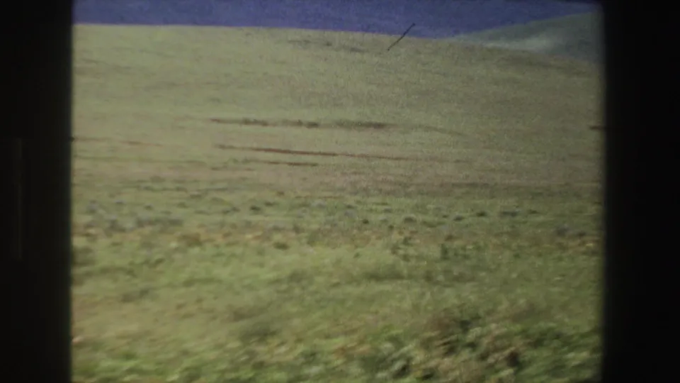 1969 South Africa 8mm frame showing rolling low grass and distant hills, with visible grain and exposure shift.