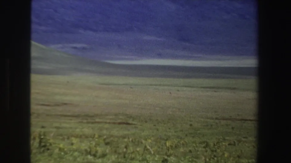 1969 South Africa landscape frame with a broad grassy valley, shadowed mountain slopes, and muted cloudy sky.