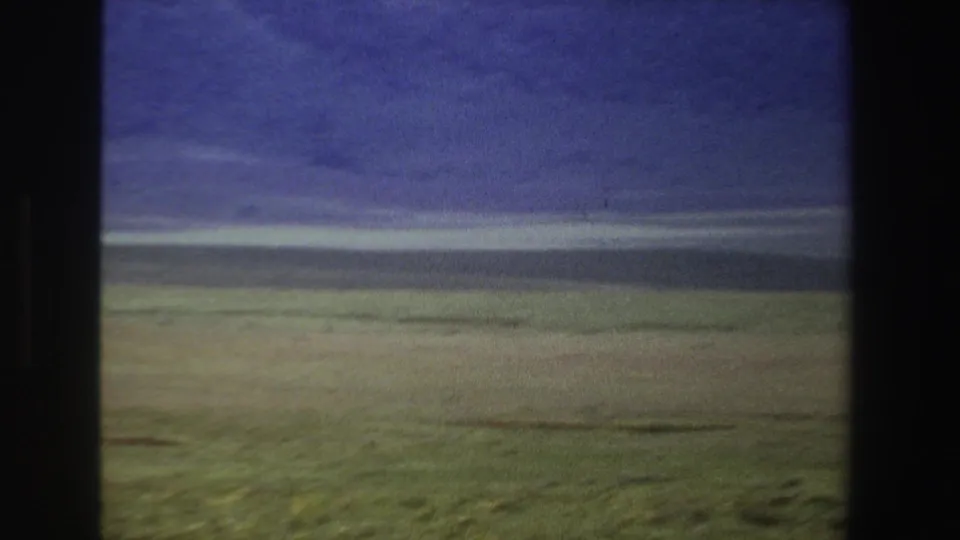 1969 South Africa 8mm frame showing a muted grassy plain, distant low ridge, and heavy blue-purple cloud cover.