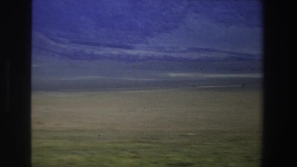 1969 South Africa home-movie frame showing a broad plain, distant dark horizon, and cool-toned cloud cover.