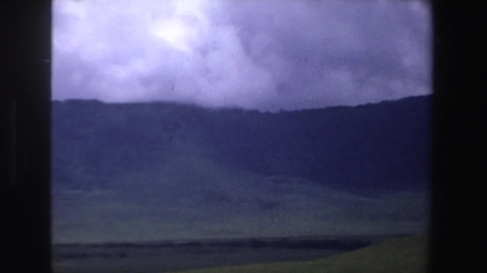 1969 South Africa 8mm frame with a dark mountain ridge, open plain, and dramatic blue-purple overcast sky.