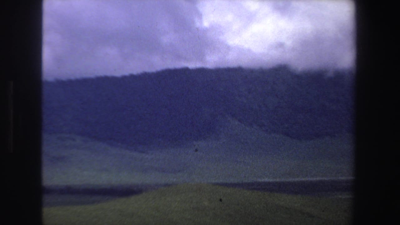 Cloudy mountain ridge above open grassland, framed by dark 8mm film borders.