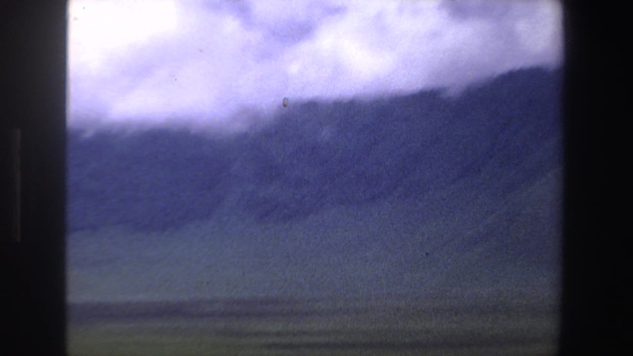 1969 South Africa travel footage frame with blue-toned mountains, open grassland, and bright overcast sky seen through 8mm borders.