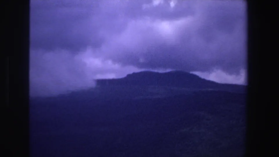 1969 South Africa 8mm frame showing a cloudy landscape with distant hills or mountains, rendered in grainy blue-purple tones.
