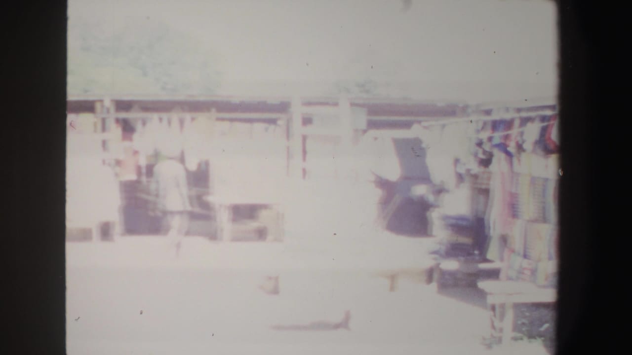 Market walkway with a person near shaded stalls and hanging textiles.