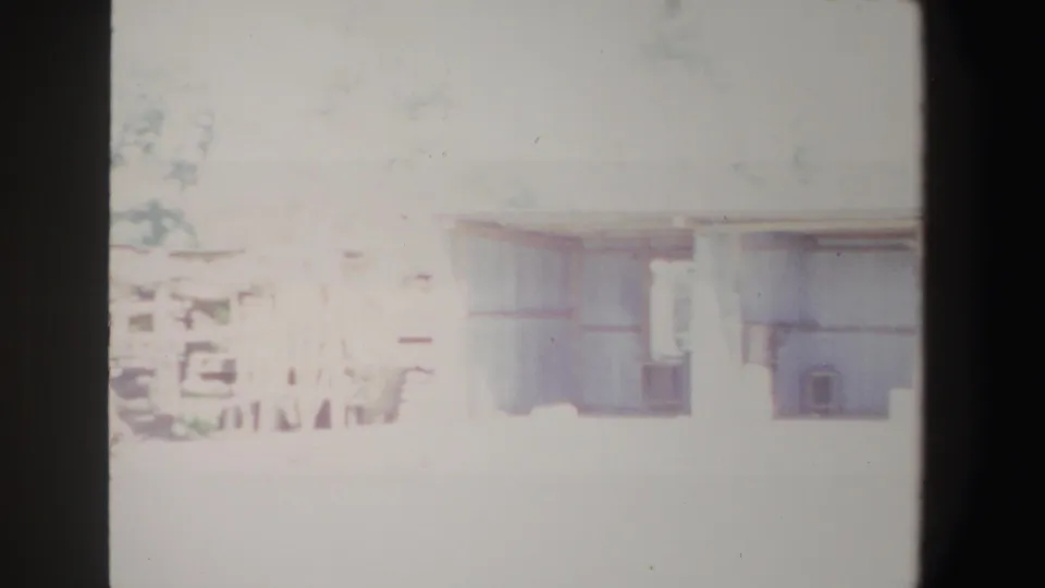 Overexposed 1969 South Africa home-movie frame of a rural house facade, porch area, windows, and trees.