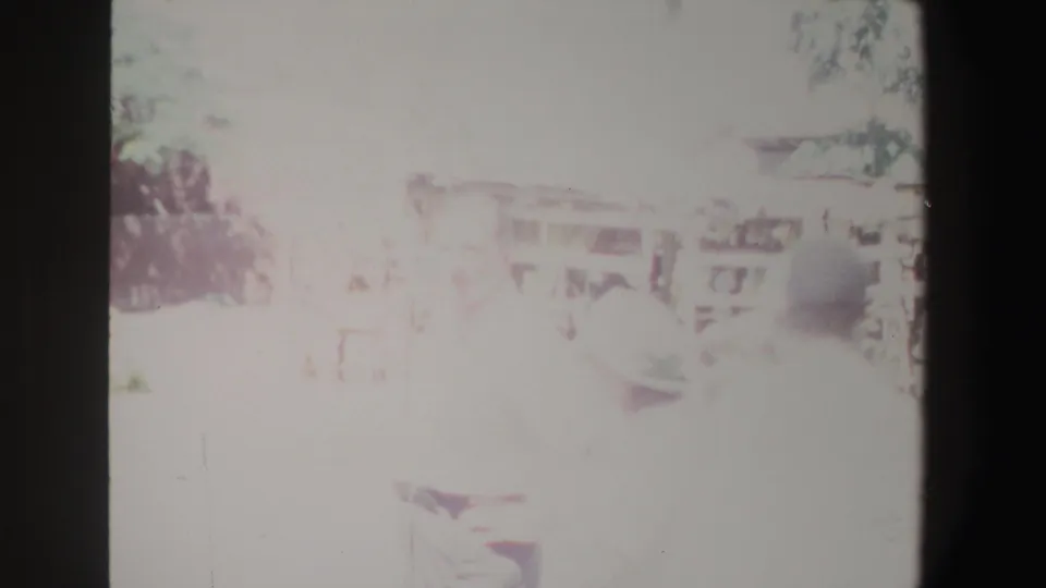 Bright 1969 South Africa home-movie frame with a rural house, yard, trees, and an indistinct person near the foreground.