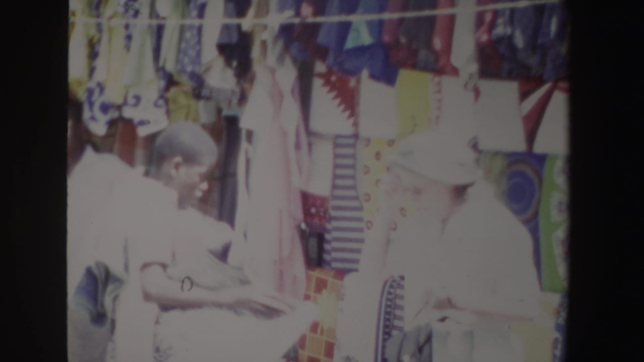 Two people stand close to hanging textiles as one holds or examines goods.