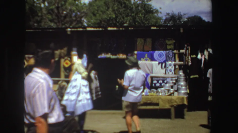 Wide 1969 South Africa market view with visitors near a textile display and shaded stall area.