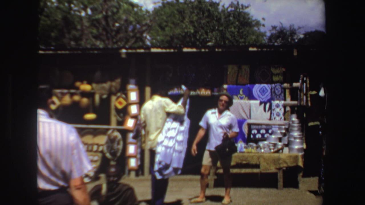 A person in a green hat walks near textile and craft displays at an outdoor market.