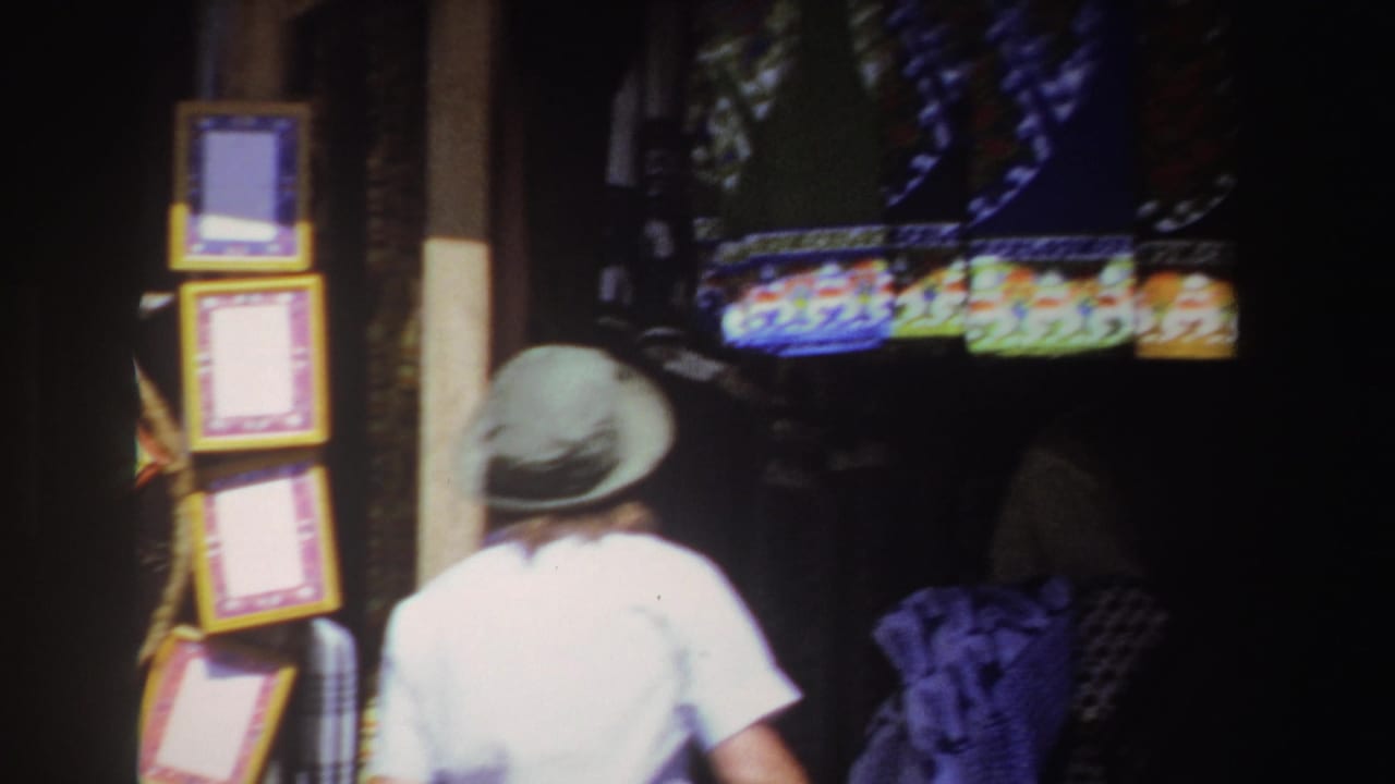 Person in a green hat stands near colorful market displays under strong daylight.