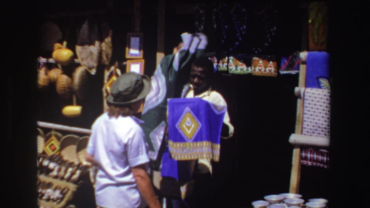 Vendor holds up fabric while a tourist watches at a market stall.