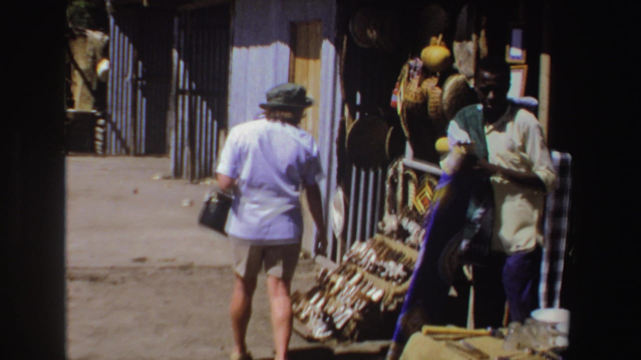 Tourist walks past a market stall displaying baskets, hats, and other crafts.