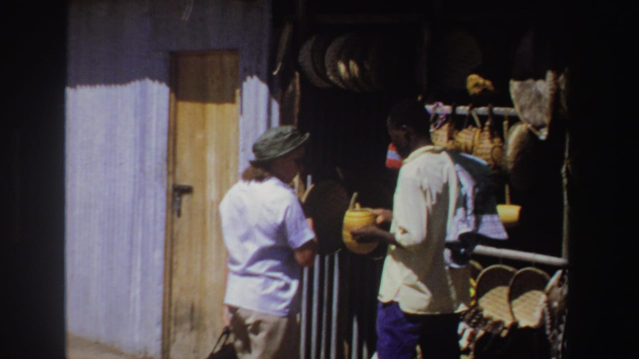 Tourist faces a vendor holding a yellow woven basket at a shaded market stall.