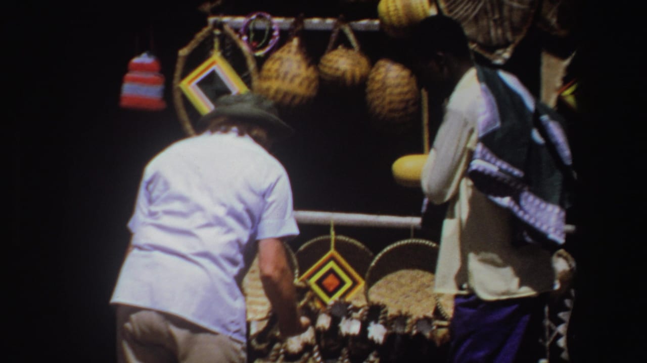 Adult men browse a South African market display with baskets, hanging craftwork, and a yellow object in bright daylight.