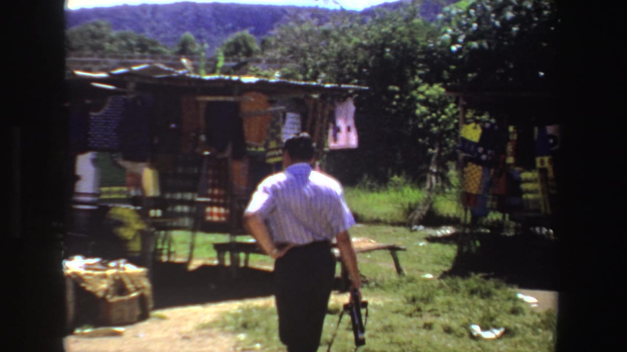 Man in a striped shirt walks toward a small outdoor clothing stall in a grassy rural area.
