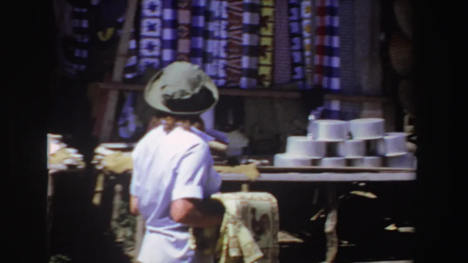 Seen from behind, the tourist approaches a market display with stacked white bowls and hanging fabrics in South Africa.
