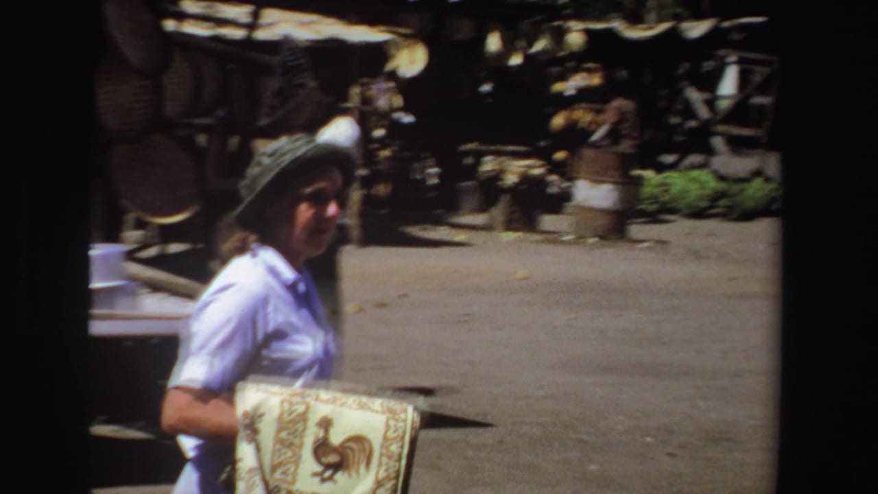 Woman carrying a patterned cloth walks through an outdoor market walkway.