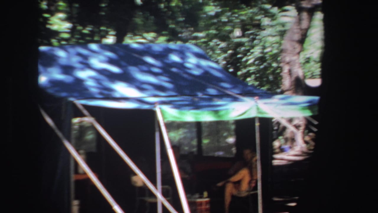 Tent canopy with white poles and a seated man visible in shade.