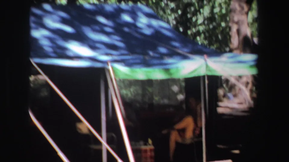 1969 South Africa 8mm frame with the camera closer to the canopy, showing poles, wooded shade, and a man seated beneath it.