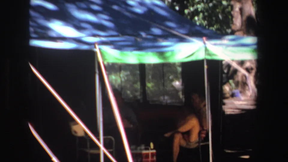 1969 South Africa 8mm frame showing a person seated inside a dim tent beneath blue and green canopy fabric.