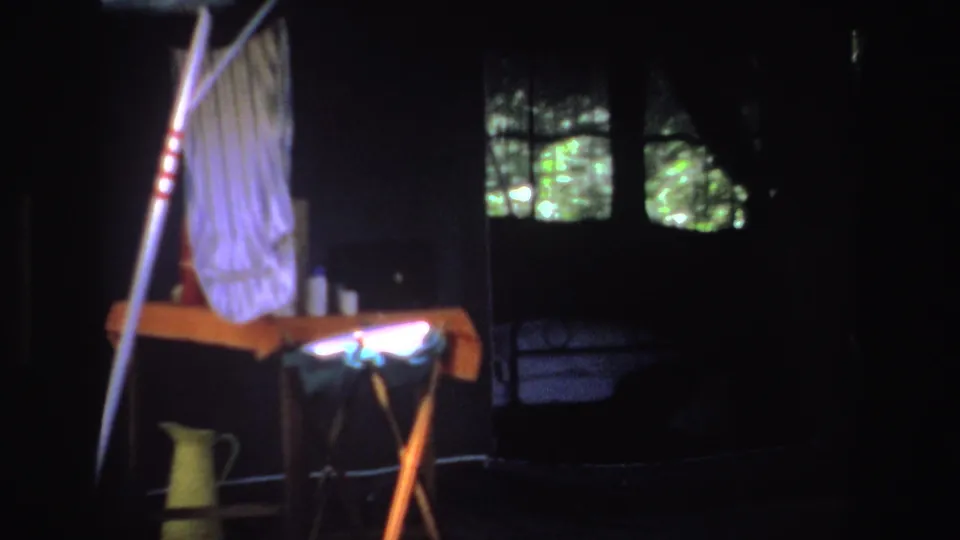 1969 South Africa home-movie frame showing a tent interior with hanging clothes, cup, and pale flask or jug.