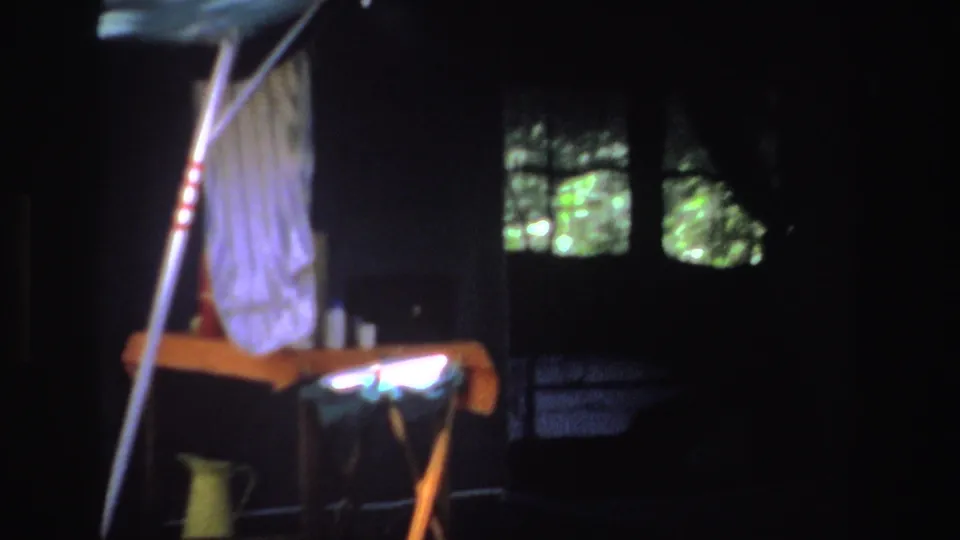 1969 South Africa 8mm frame with a shaded campsite setup, tent poles, hanging fabric, a table covering, and greenery visible through dark openings.