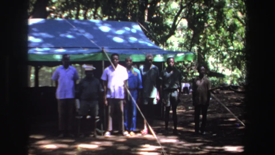 Men stand close together near a shaded tarp shelter, with 1969 South Africa context supplied by the clip metadata.