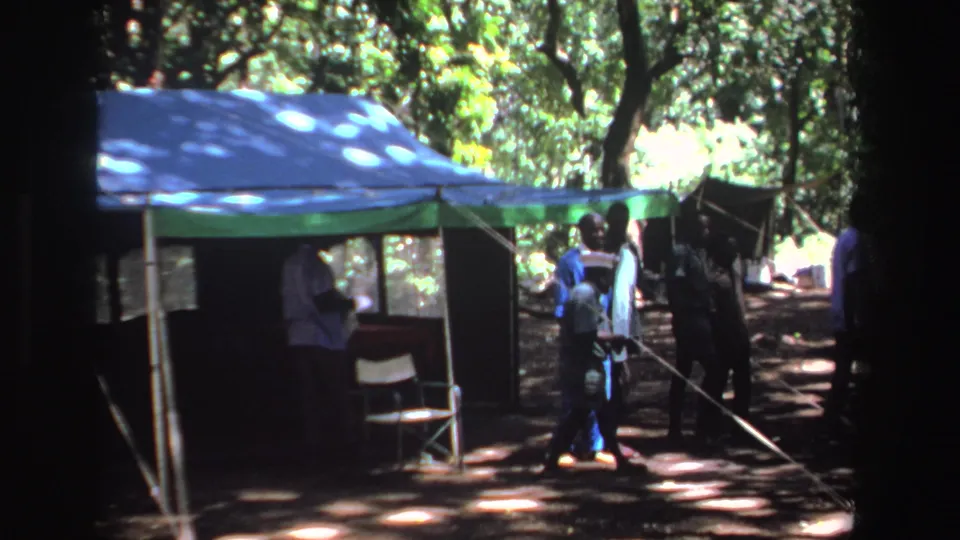 People in casual clothing gather near a shaded canopy tent in wooded South Africa, supported by 1969 metadata.
