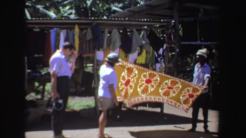 A South Africa bazaar scene shows visitors watching as a vendor presents a red-and-gold patterned tablecloth.