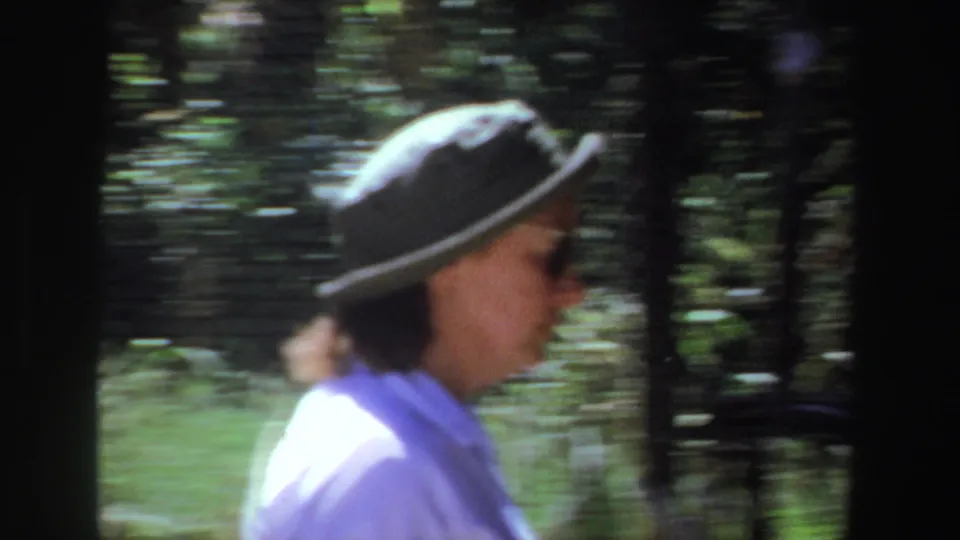 A side view shows the woman in her green hat walking through a shaded outdoor market area, with blurred trees behind her.