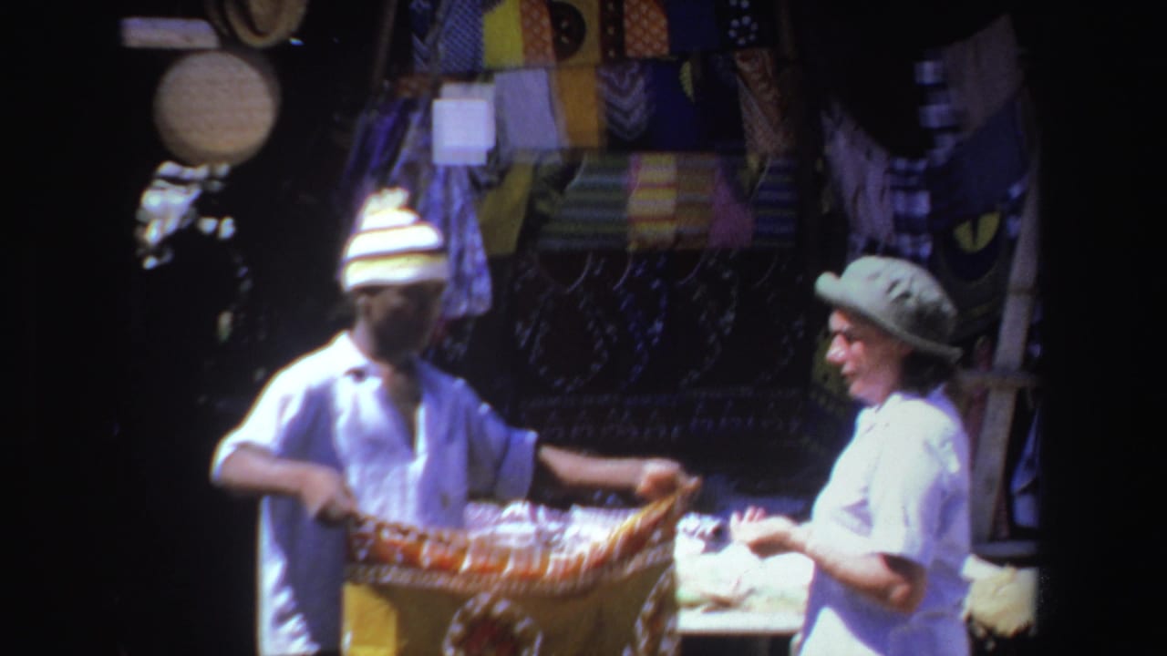 Vendor and tourist hold a colorful woven textile at a market stall.