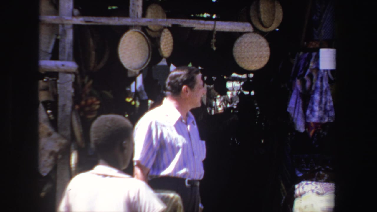 Tourist stands near hanging baskets while a person passes in the foreground.