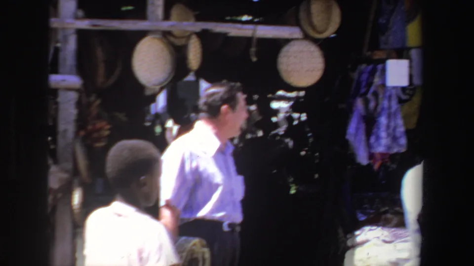 1969 South Africa 8mm frame showing a tourist moving past a craft stall with hanging baskets and textiles.