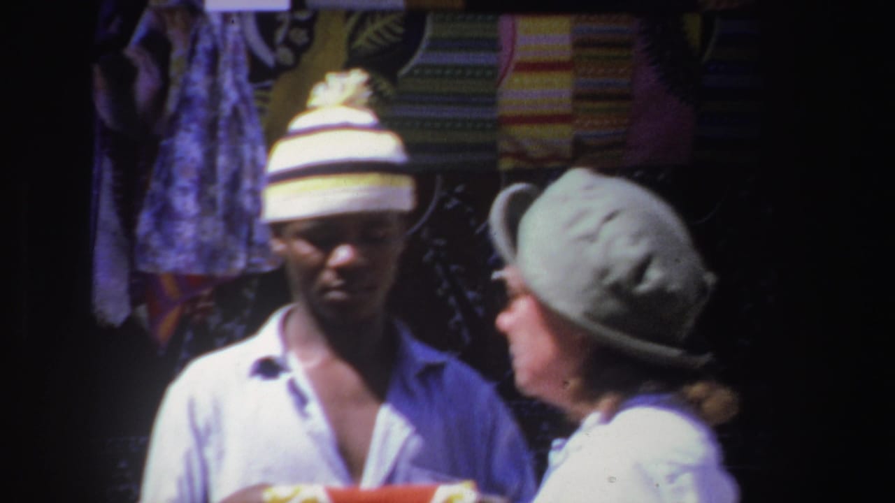Man in striped knit hat faces a woman in a green hat near hanging fabrics.