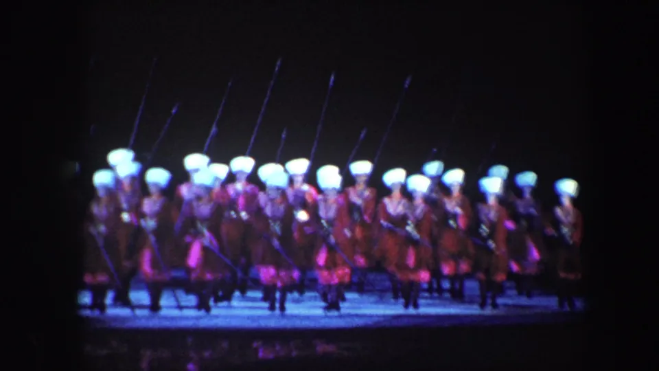 Costumed performers in Baltimore, 1960, move in formation with long pikes under blue and purple stage lighting.