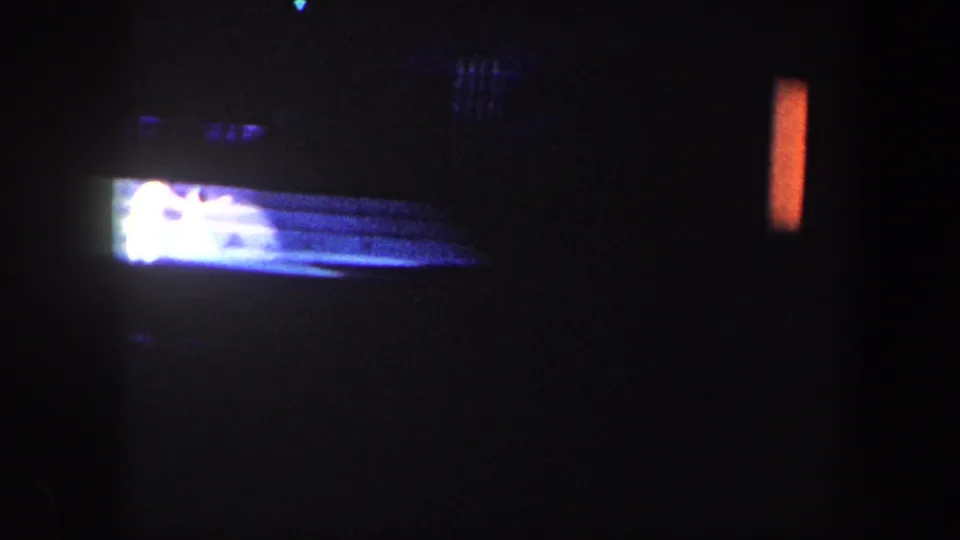 Low-light 8mm frame from the stage show, with a bright performer or prop near the floor against a dark theater background.