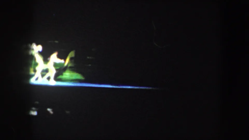1960 Baltimore home-movie frame showing distant dancers in bright green and white light against a dark stage.