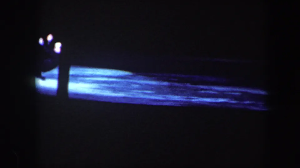 Two figures are visible near a pool of blue stage light in this dark 1960 Baltimore home-movie frame.