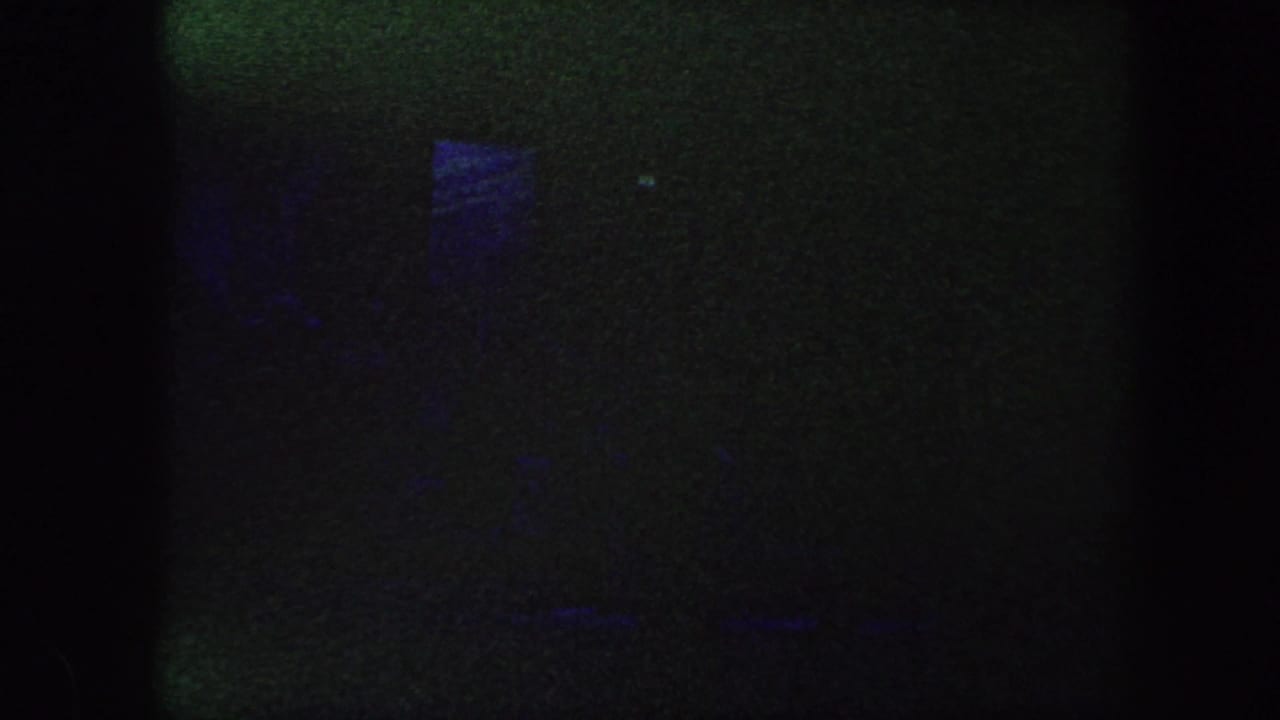 1960 Baltimore 8mm frame showing a mostly dark performance stage with blue illumination and indistinct shapes.
