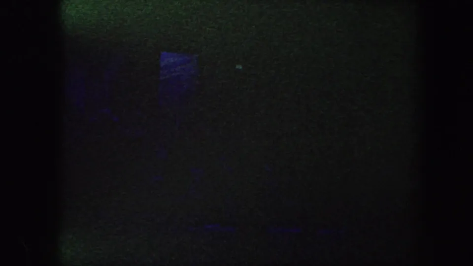 1960 Baltimore 8mm frame showing a mostly dark performance stage with blue illumination and indistinct shapes.