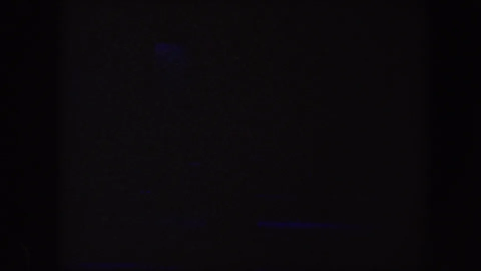 Low-light 8mm frame from the Baltimore circus footage with only small colored stage lights visible.