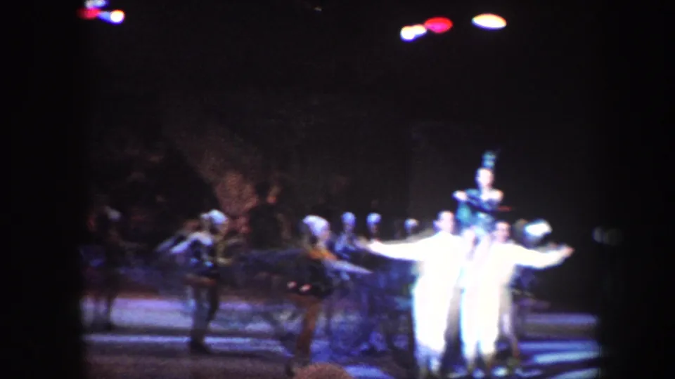 1960 Baltimore home-movie frame of circus performers and acrobats under spotlights, with a central figure in white.